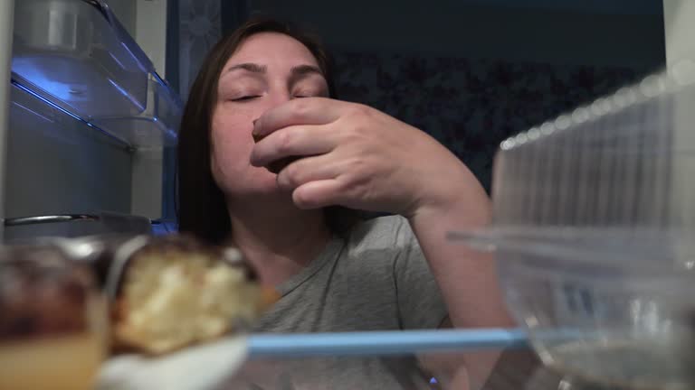 Smiling woman opens refrigerator to eat tasty bun at night