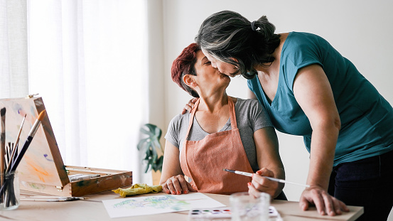 Senior artist gay couple painting watercolor canvas at art home workshop - LGBTQ Lesbian mature women kissing - Small family business concept