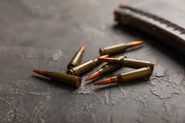 Photo of Bullets and ammo magazine on black textured marble. Bullets of a kolashnikov assault rifle close-up with space for text. Cartridges for a rifle and a carbine on a wooden background. Military concept.