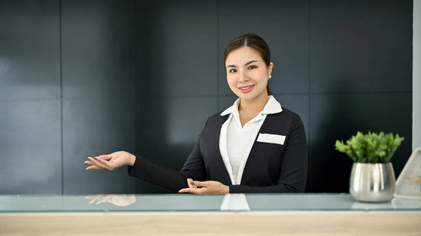 istock Friendly and attractive Asian female receptionist in a uniform stands at a front desk 1491453726