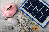 flache-komposition-mit-sonnenkollektor-led-lampe-hausmodell-geld-und-sparschwein-auf-grauem.jpg?b=1&s=170x170&k=20&c=_5YGfRHstjAh5VelCSLYDZoWo2d66Eadl0KzXIuqcs0=