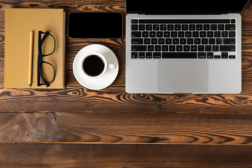 Modern workspace. Laptop with coffee cup, smartphone, glider and glasses. Copy space mockup on brown background. View from above. Flat style.