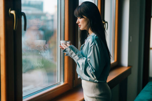 istock Young woman drinking coffee and looking through the window 1491457749