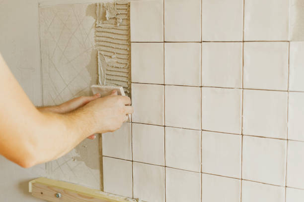 istock Worker installing stylish white tiles on plaster wall in sunlight. Hands laying modern square tile on adhesive close up. Kitchen or bathroom renovation, home improvement 1491459601