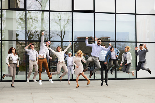 Large group of cheerful business colleagues having fun while jumping in front of an office building. Copy space.