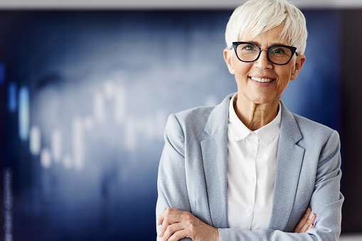 Close-up portrait of happy successful influential senior gray-haired Asian business woman, top manager, lawyer, real estate agent, standing at office, in stylish wear, looks at camera, smiles friendly