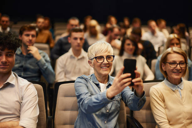 Happy senior woman using mobile phone on a seminar in board room.