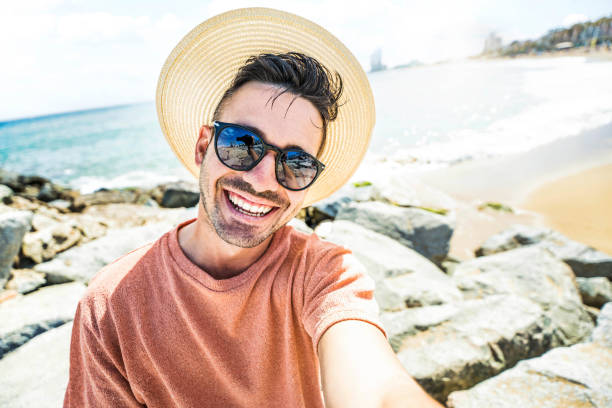 istock Handsome young man taking selfie with smart mobile phone device outside - Cheerful tourist enjoying summertime at the beach - Life style, traveling and technology concept 1491461958