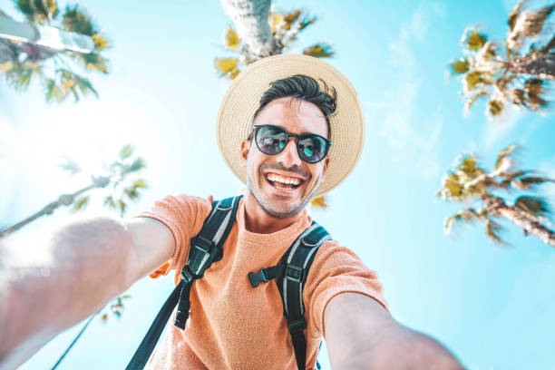 Happy tourist taking self portrait outside with cellphone on summer vacation - Handsome young man laughing at camera enjoying summertime day out - Tourism, traveler life style and technology concept stock photo