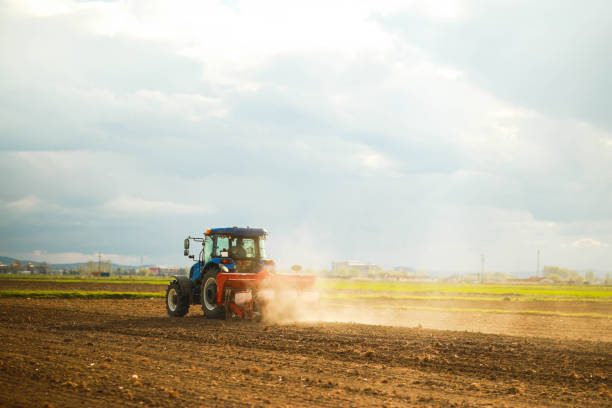 Silhouette of a tractor with a seeder against a bright sunset sky with dramatic clouds, depicting rural life and farming.