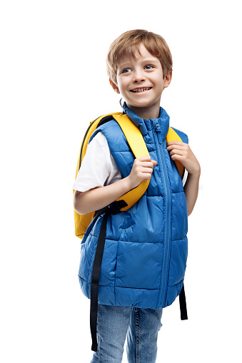 Cheerful little boy wearing yellow backpack looking away on white background. Back to School. Smiling kid