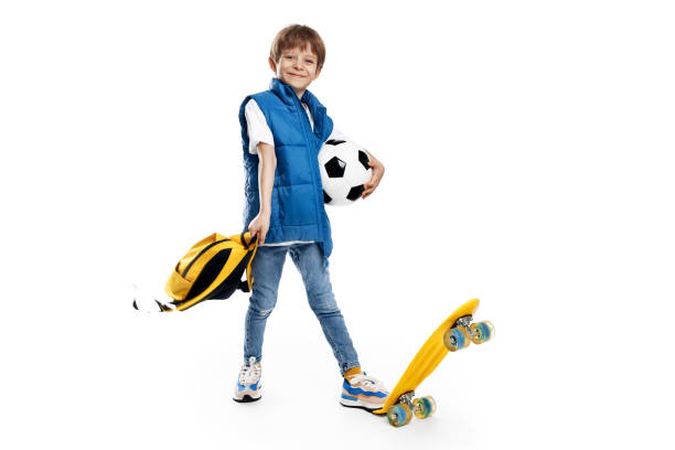 istock Dynamic image of a little boy with skateboard and backpack holding soccer ball on white background. Back to School. 1491465949