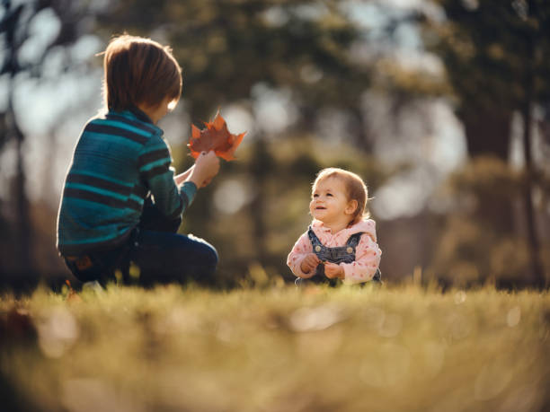 Happy baby girl enjoying with her brother in autumn day. Cute baby girl spending an autumn day with her older brother in the park. Photographed in medium format. Copy space. babyhood stock pictures, royalty-free photos & images