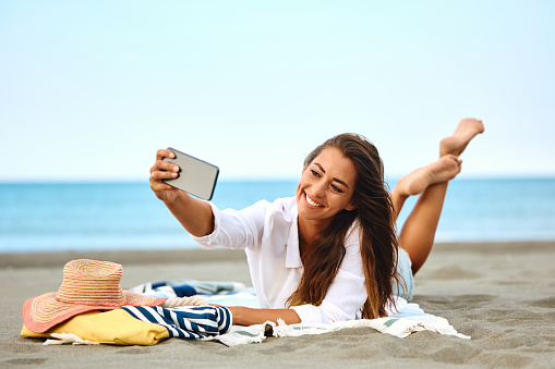 Carefree woman taking selfie while relaxing on the beach during summer vacation. Copy space.