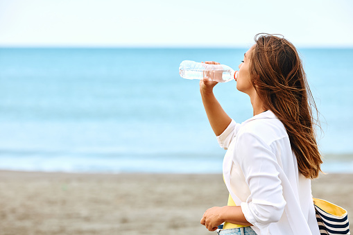 Thirsty woman drinking water on the beach. Copy space.