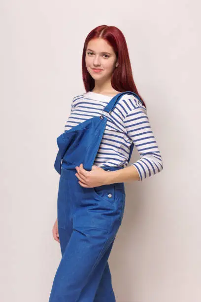 Photo of girl in a blue denim overalls and a striped blouse on a white isolated background.