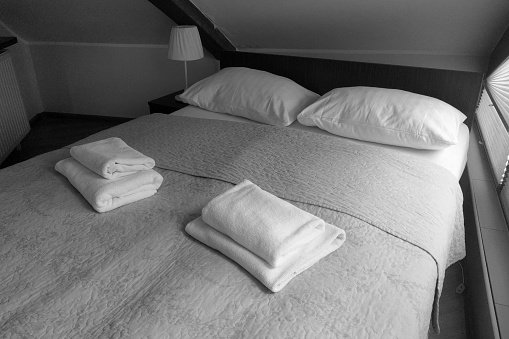 Black and white photo. Clean towels on the bed in the room