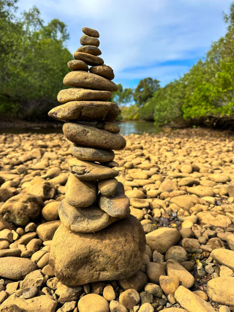 istock Rock Cairn stack with river rocks down by the rivers edge.  Water & green trees in the distance. Blue cloudy sky - Gold Coast Queensland Australia 1491473713