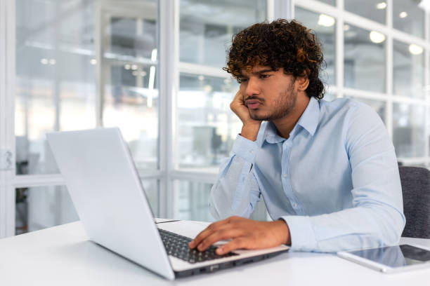 istock Upset thinking businessman working with laptop inside modern office, man frustrated solving difficult decision at workplace, hispanic man with curly hair serious in shirt 1491473902