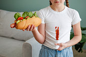 The child stained his clothes with ketchup. A girl eats a hot dog.