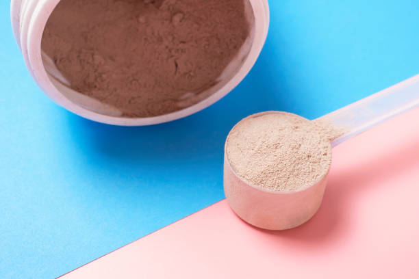 istock Chocolate protein powder in scoop and plastic jar on pink and blue background. 1491474317