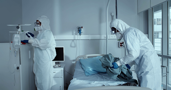 Medical staff in protective suit and mask disinfecting hospital room during corona virus. Nurses in ppe suit cleaning furniture and making bed in hospital ward