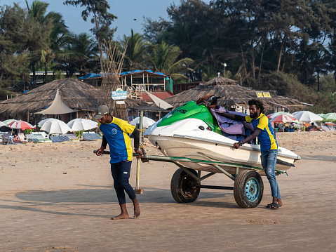 Calangute, Goa, India - January 2023: Two men hauling a boat on a cart across the beach in Calangute in Goa.
