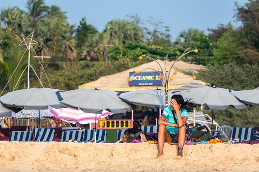 Calangute, Goa, India - January 2023: A female Caucasian tourist sitting alone on the beach outside a shack.