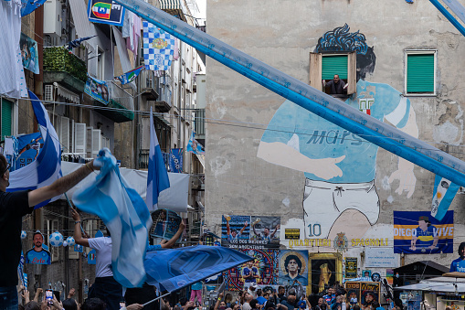 Naples, Italy - May 5, 2023: Fans of the Napoli football team celebrate the victory of the Italian championship in the street. Euphoric people flock to the Spanish quarters in front of the Maradona mural.