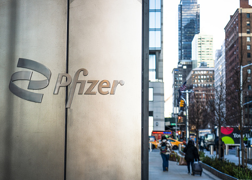 New York City, USA - Pedestrians on the sidewalk of a street in Midtown Manhattan, passing Pfizer's headquarters building, with the company name in close-up on an external wall of the building.