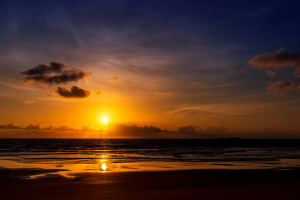 Breathtaking view of the sun gently setting on the beach with its reflection shining in the sea water