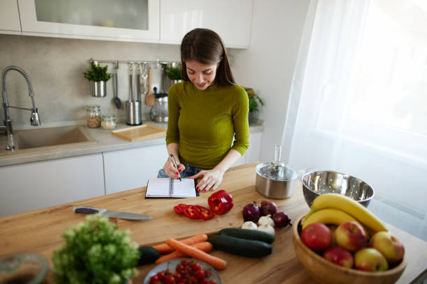 istock Young woman reading cookbook in the kitchen, looking for recipe 1491486536