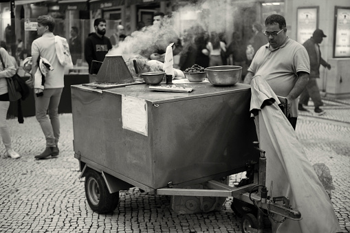 Lisbon, Portugal - October 29, 2022: A traditional roasted chestnuts vendor wait for clients  at the Rua Augusta street in Lisbon downtown.
