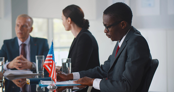 Interracial partners working and discussing together business plan at meeting in office. Afro-american businessman sitting at conference room and writing notes at corporate meeting