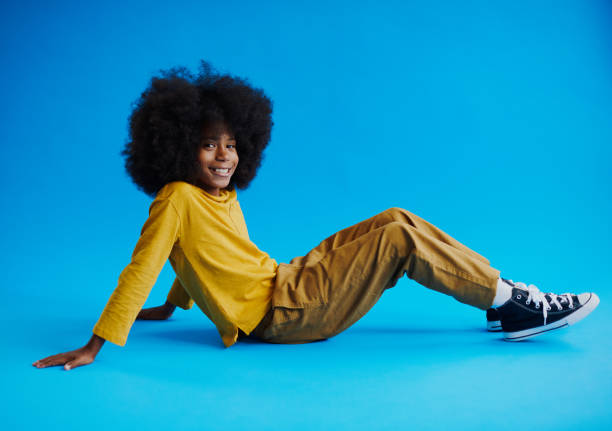 istock Young black boy with a afro sitting on the floor, smiling into the camera with copy space. Stock photo 1491497358