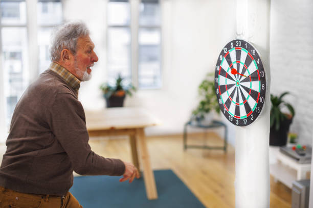 istock A modern senior man is playing darts at home and aiming the target. 1491497522
