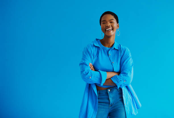 young black woman standing with her arms crossed, laughing looking at the camera wearing casual clothing with copy space stock photo - smiling clothing garment lifestyles imagens e fotografias de stock