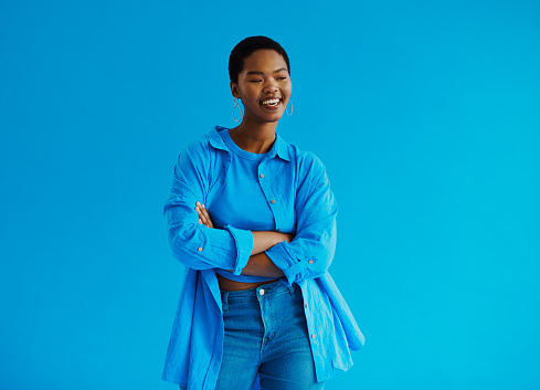 Young black woman standing with her arms crossed, smiling looking away from the camera wearing casual clothing, shot against a blue background with copy space stock photo