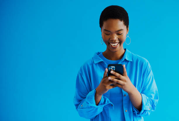 立って携帯電話を見ている若い黒人女性、コピー用スペース付きのカジュアルな服を着てテキストメッセージに返信しながら微笑む、ストック写真 - technology mobile phone clothing smiling ストックフォトと画像