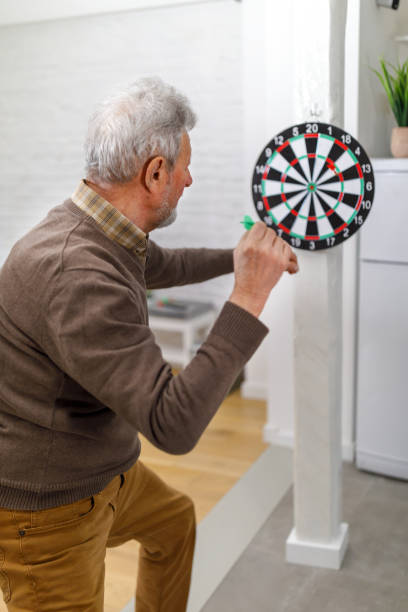 istock A modern senior man is playing darts at home and aiming the target. 1491498907