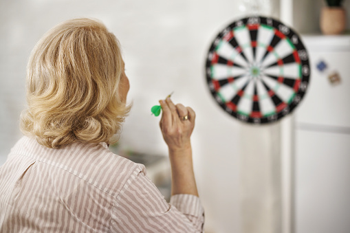 An older woman is having a party at home and enjoying playing a dart game.
