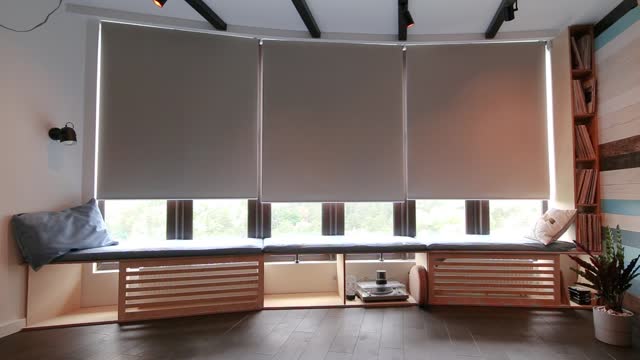 Automatic roller blinds beige color close down on big glass windows.