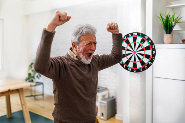 un uomo anziano sta giocando a freccette nel suo appartamento di casa e festeggia la vittoria. - dartboard photography competition sports and fitness foto e immagini stock