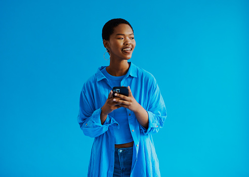 Young black woman standing and looking away from the camera whilst smiling with a mobile phone in her hand with copy space stock photo