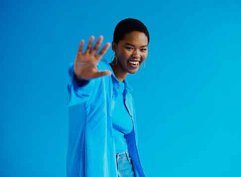 Young black woman reaching for the camera whilst smiling wearing a blue shirt and blue top with a jeans with copy space, stock photo