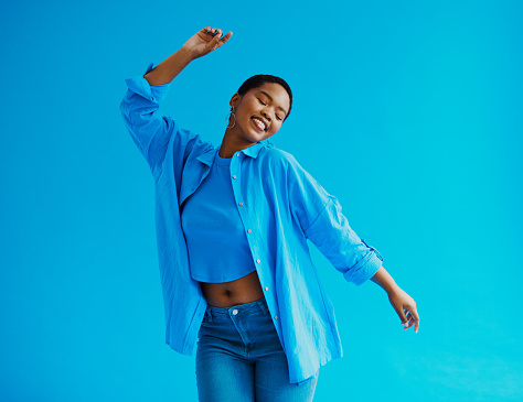 Young black woman wearing a jean, blue shirt and blue top whilst dancing and smiling shot against a blue background with copy space stock photo