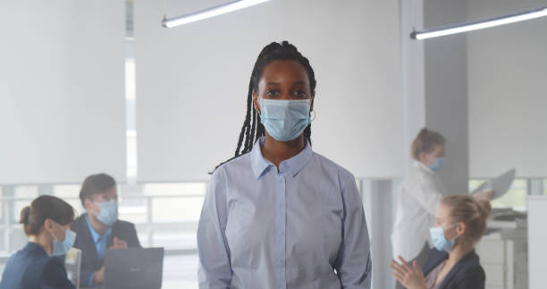 une femme afro-américaine debout au bureau devant l’équipe et portant un masque facial - black crowned photos et images de collection