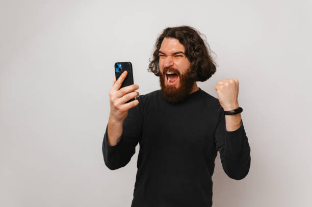 istock Bearded man shouts while looking at the phone and making the winner gesture. 1491499932