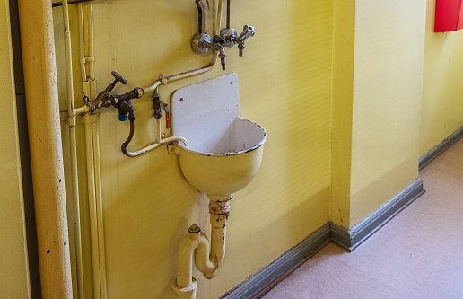 Metal sink and water taps against a yellow wall. 20th century system. Prison in Finland