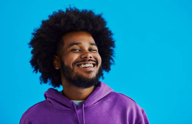 Young black man with a afro hairstyle looking into the camera whilst having his face turned to see the side of his face, smiling with copy space, stock photo